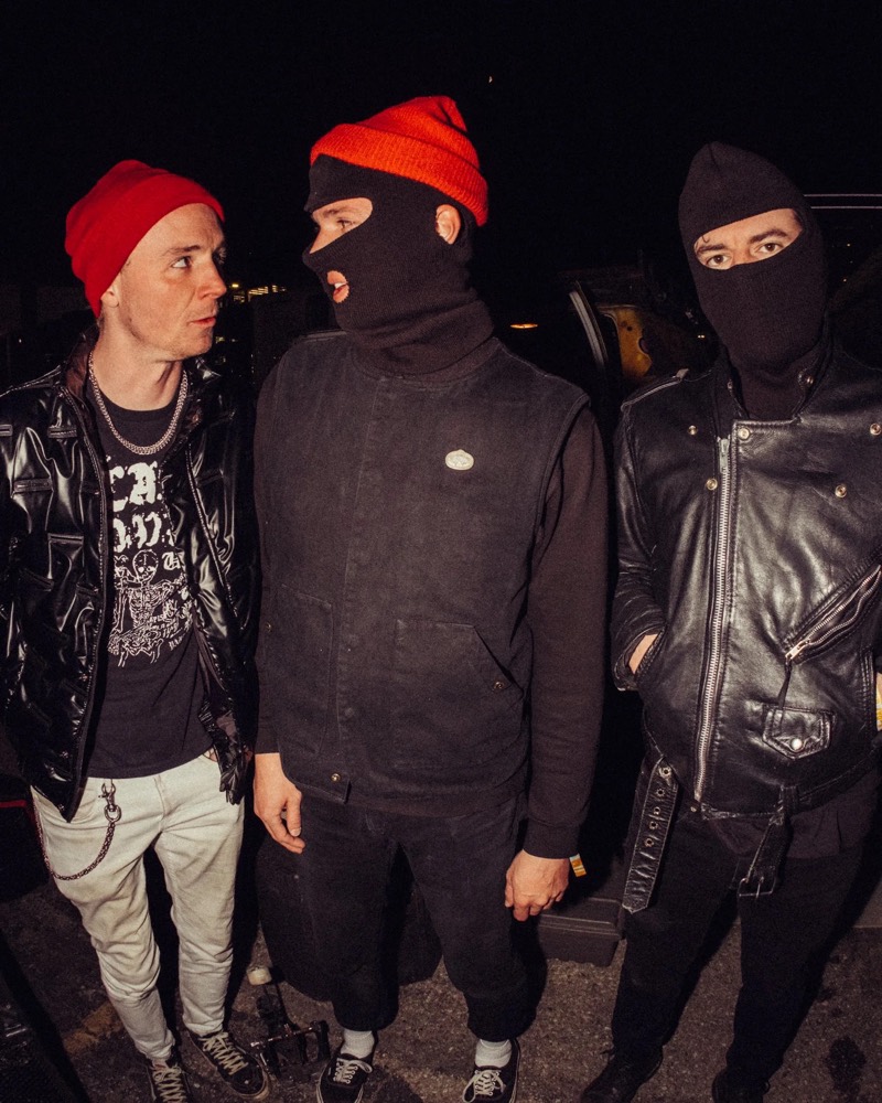 Three people in balaclavas and red beanies photographed at night with direct flash