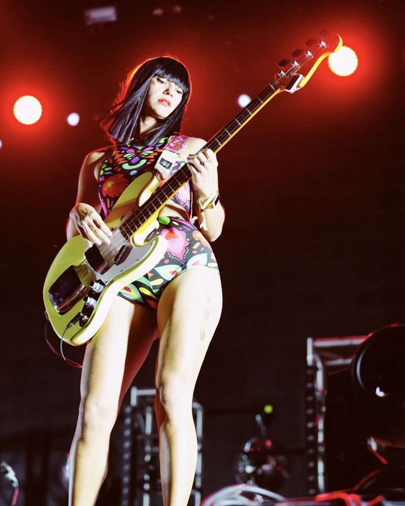 A bass player in a patterned bodysuit under red stage lights