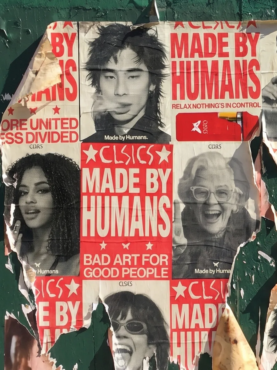 Torn CLSICS "Made by Humans" wheatpaste posters on a green plywood wall