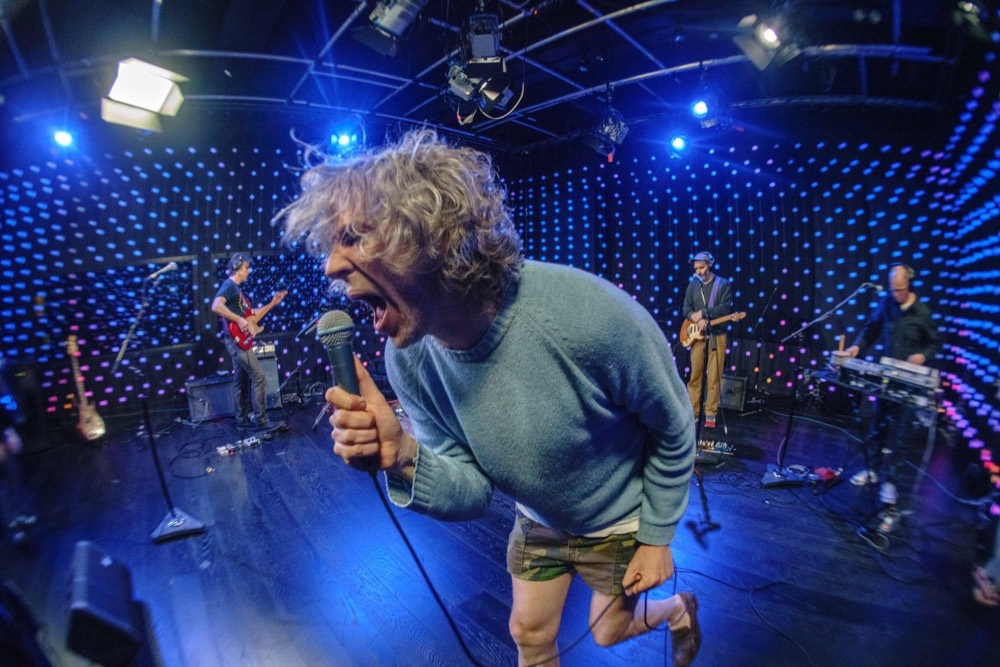 A singer mid-performance on a studio stage backed by a wall of blue LEDs