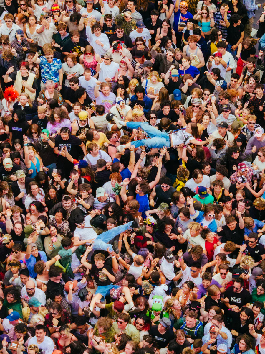 A packed festival crowd seen from above, with two people crowd surfing across it