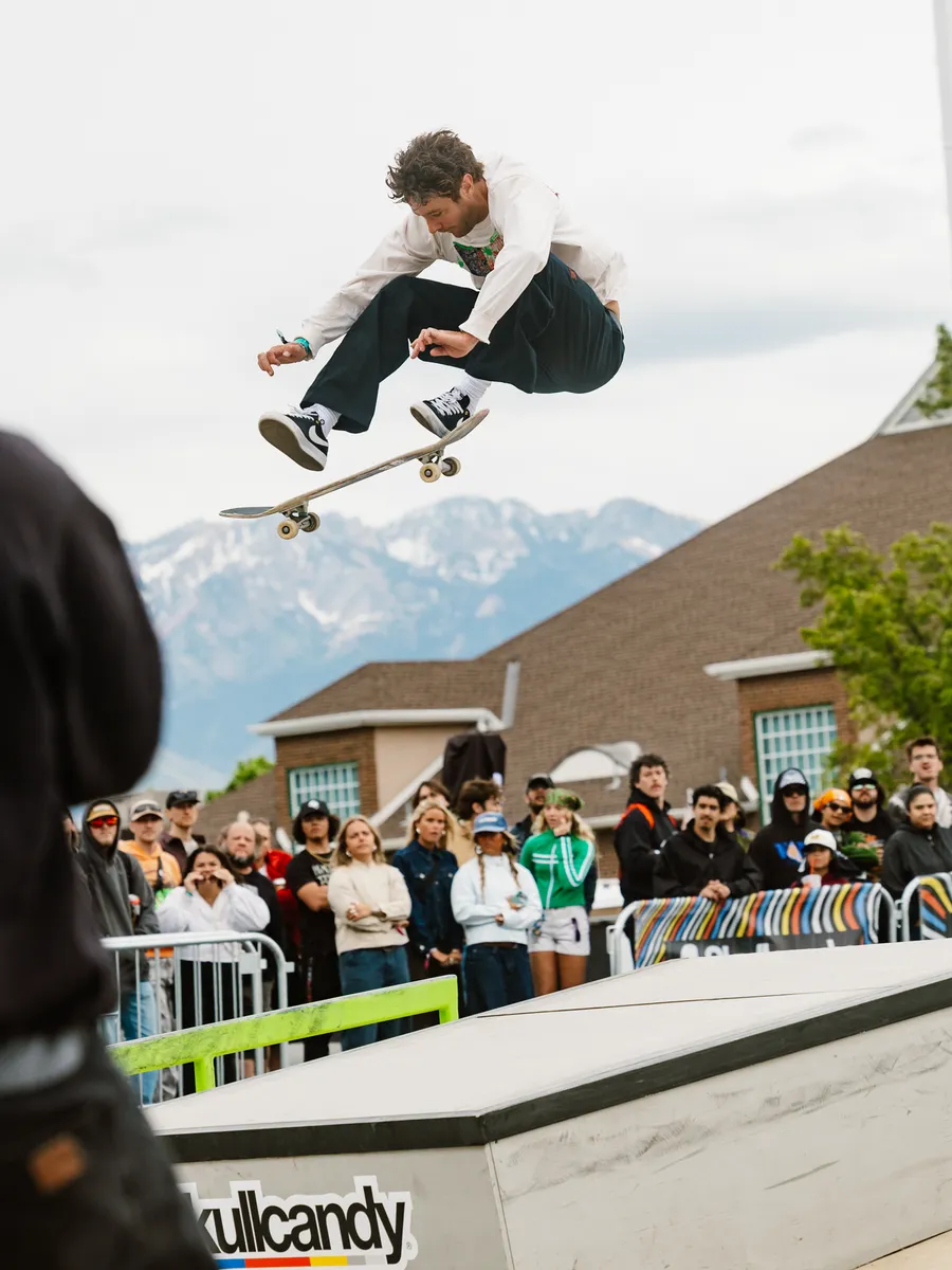 A skater launches high over a ramp at the festival skate contest, a crowd watching behind the barriers and mountains beyond