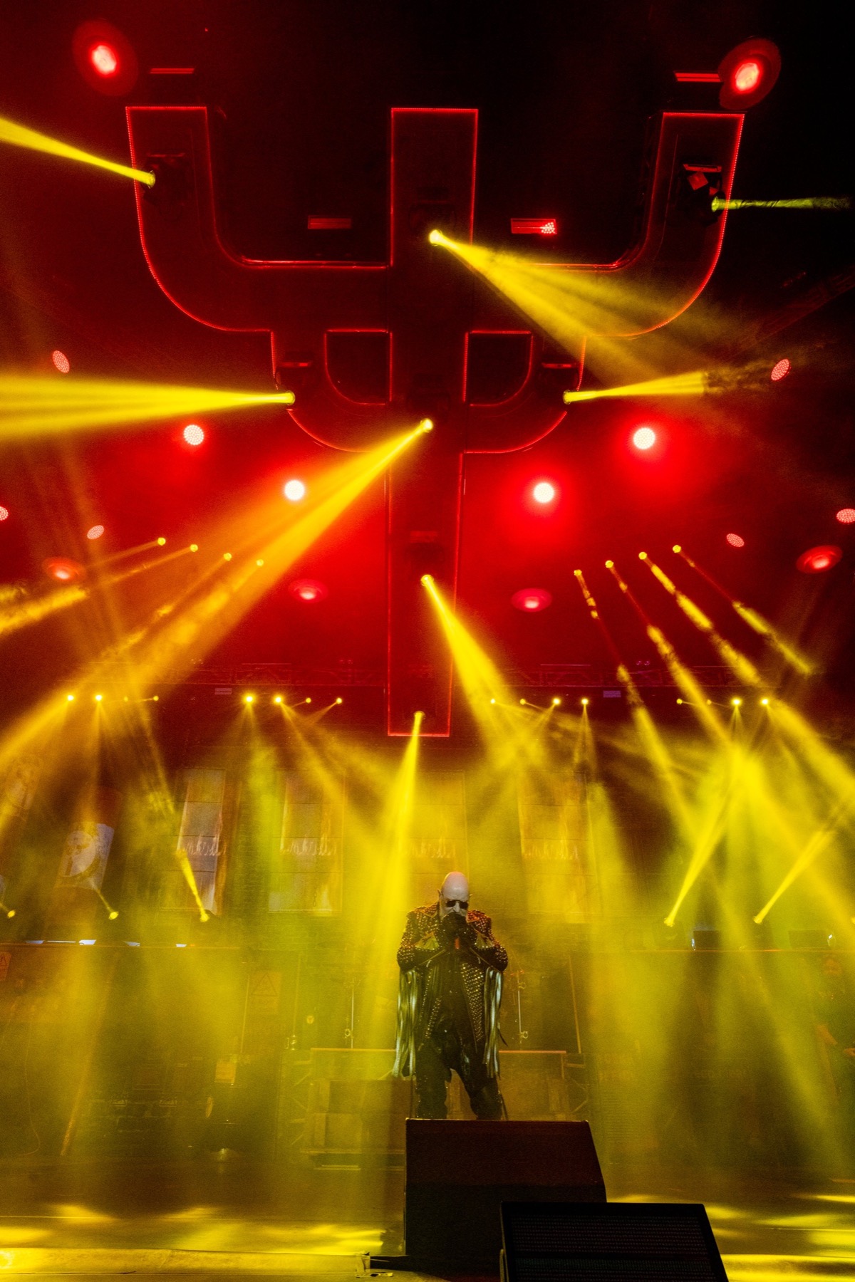 A performer alone on a large stage under crossing yellow and red light beams