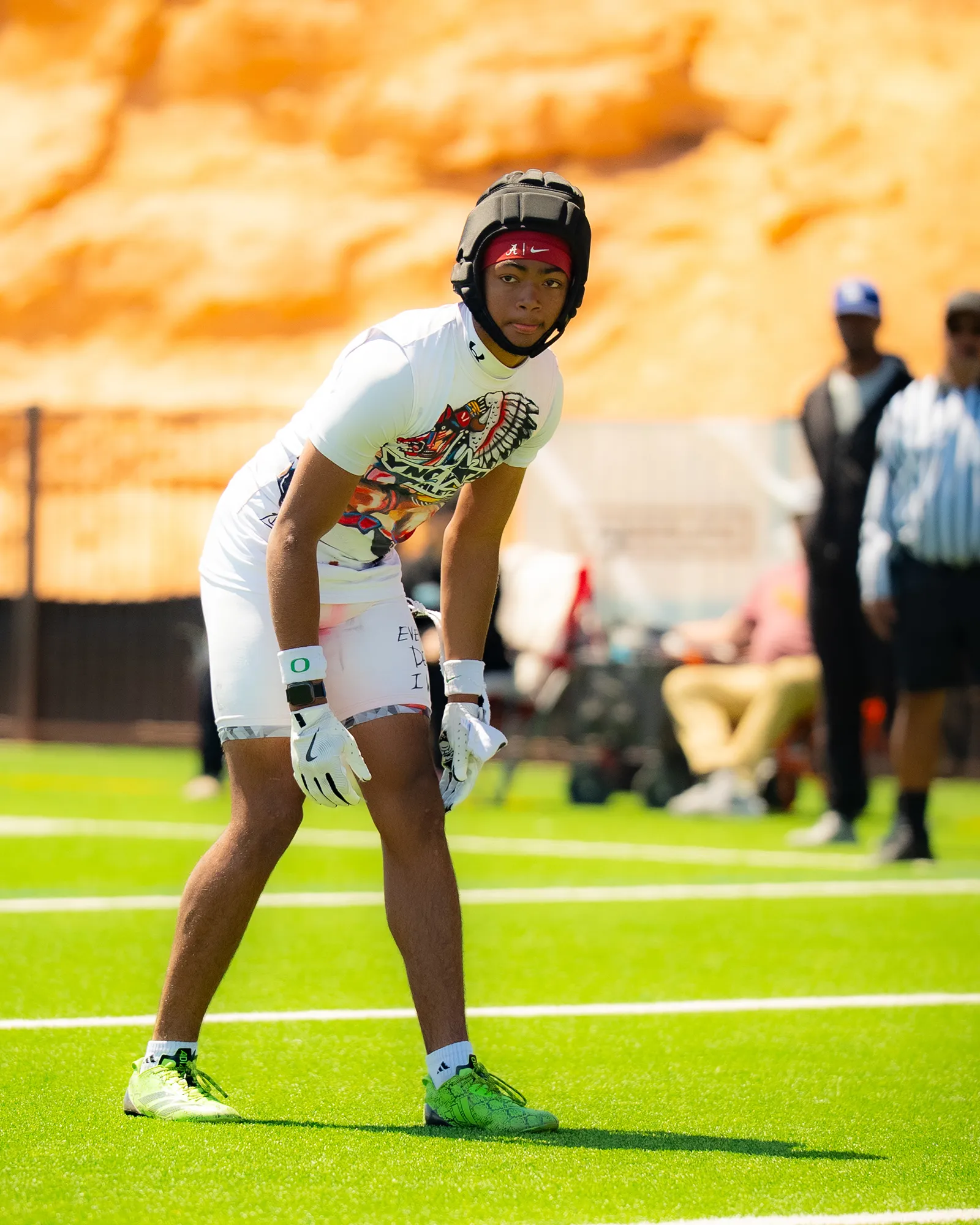 A young athlete in a helmet and white YNGSTAR kit crouches ready on the turf, an orange rock wall behind